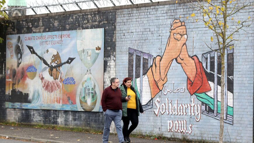 People pass a pro-Palestinian mural on the Republican Falls Road in Belfast on October 23, 2023. Northern Ireland may be thousands of miles from the Middle East but signs of the current heightened conflict can be seen on the streets of the British province. Palestinian and Israeli flags flutter in pro-Irish and pro-UK neighbourhoods in Northern Ireland, tapping into its own history of conflict and division that still affects everyday life despite a 1998 peace deal that largely ended violence. (Photo by Paul