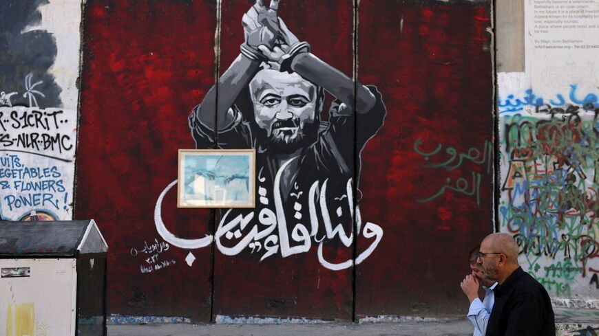 Men walk past a section of Israel's separation barrier painted with a portrait of Palestinian Marwan Barghouti, held in an Israel jail, on November 6, 2023 in Bethlehem in the occupied West Bank.