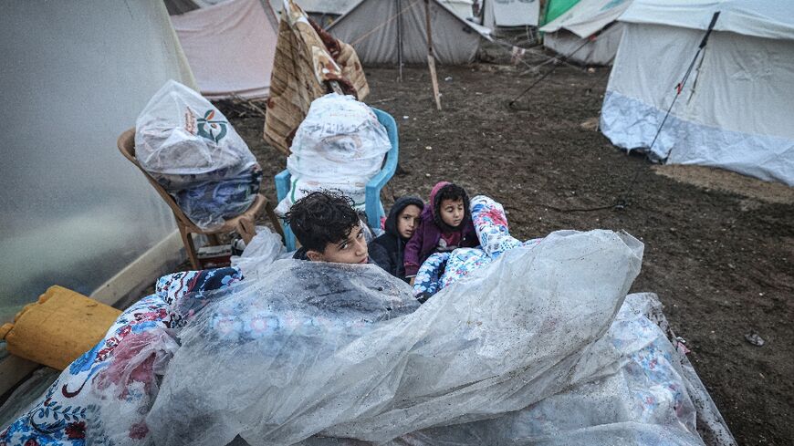 Young Palestinians sit outside on mattresses covered with plastic at a camp for displaced people in Rafah, in the southern Gaza Strip 