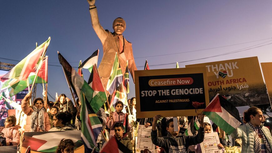 People raise flags and placards as they gather around a statue of late South African president Nelson Mandela to celebrate a landmark "genocide" case filed by South Africa against Israel at the International Court of Justice, in the occupied West Bank city of Ramallah on January 10, 2024.