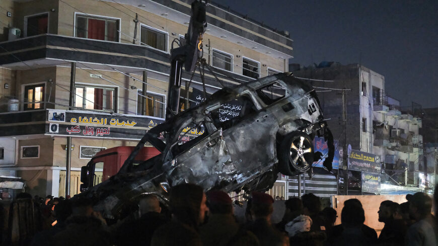 People watch as a vehicle that was hit by a drone strike, reportedly killing three people including two leaders of a pro-Iran group, is carried away in Baghdad on Feb. 7, 2024. 