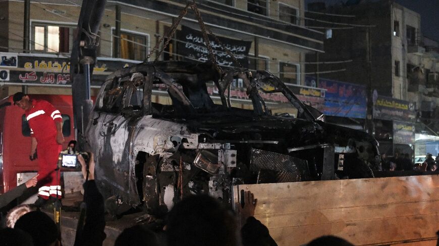 People watch as a vehicle that was hit by a drone strike killing three people including two leaders of a pro-Iran group is removed from a Baghdad neighbourhood