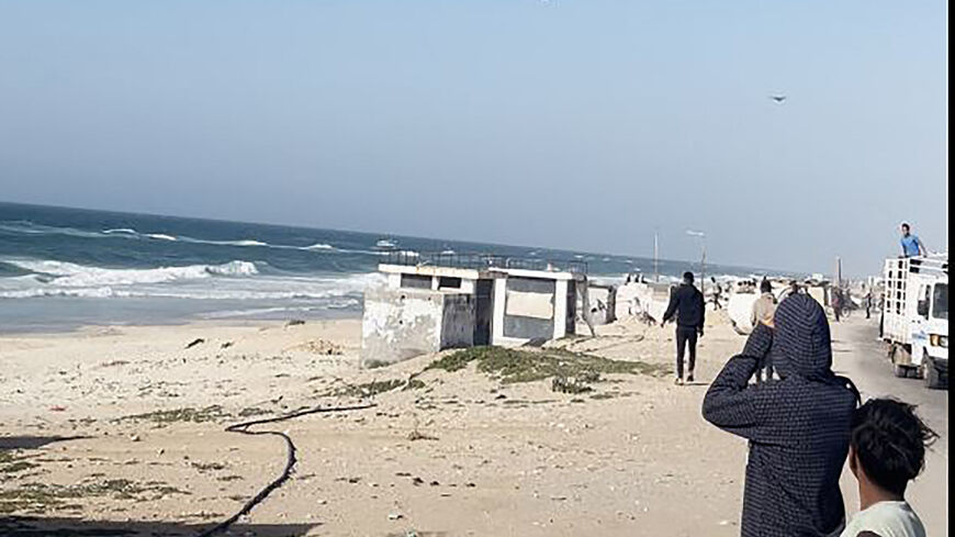 In this image grab from an AFPTV video, people watch as a US aircraft carrying food parcels flies above a beach in the Gaza Strip before dropping the humanitarian aid attached to parachutes, on March 2, 2024. Israel's top ally the United States said it began air-dropping aid into war-ravaged Gaza on March 2, as the Hamas-ruled territory's health ministry reported more than a dozen child malnutrition deaths. (Photo by AFP) (Photo by -/AFP via Getty Images)