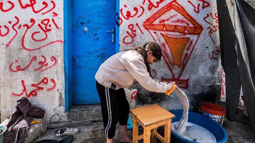 A girl washes clothes by hand at a camp for displaced Palestinians erected in a school run by the United Nations Relief and Works Agency for Palestine Refugees (UNRWA) in Rafah in the southern Gaza Strip on March 13, 2024