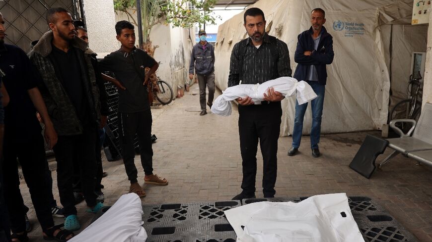 Outside the morgue of a hospital in Rafah, the southern Gaza Strip, a man carries the shrouded body of a child killed in Israeli bombardment