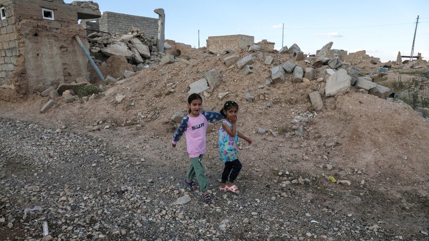 Iraqi Yazidi children walk near buildings that were destroyed during the 2014 attack by Islamic State group