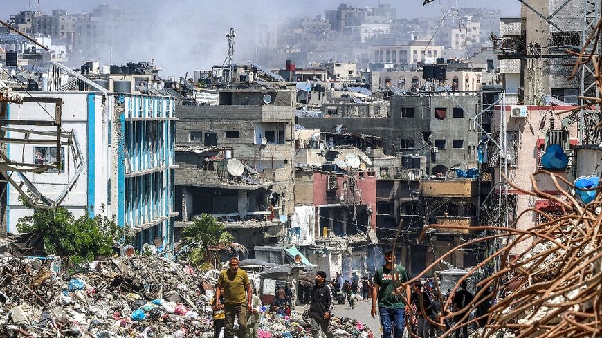 People walk past a mound of trash and destroyed buildings as smoke rises during Israeli bombardment in Jabalia, northern Gaza