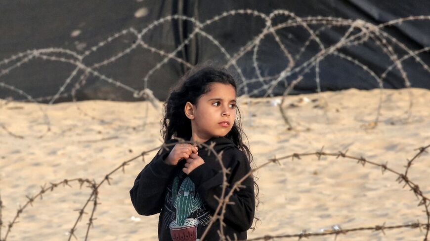 A girl stands behind barbed wire at a camp for displaced Palestinians in Rafah in the southern Gaza Strip on April 30, 2024