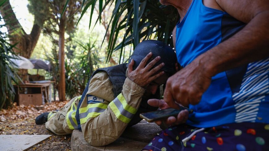 An Israeli firefighter and a resident take cover as sirens sound to warn of rockets launched from southern Lebanon, amid near-daily cross-border clashes