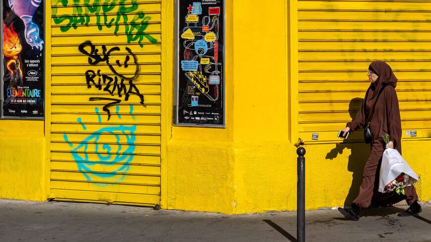 A woman wearing a hijab with a bouquet of flowers in her hand walks down a street in the Barbes district in Paris on June 25, 2023.