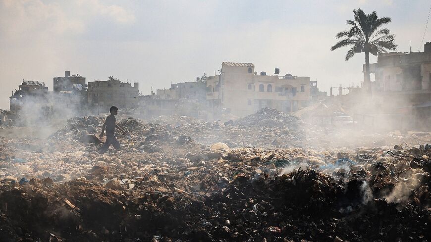 A Palestinian youth walks past piles of smouldering waste at Al-Maghazi Palestinian refugee camp, central Gaza, in the absence of municipal services during the Israel-Hamas war