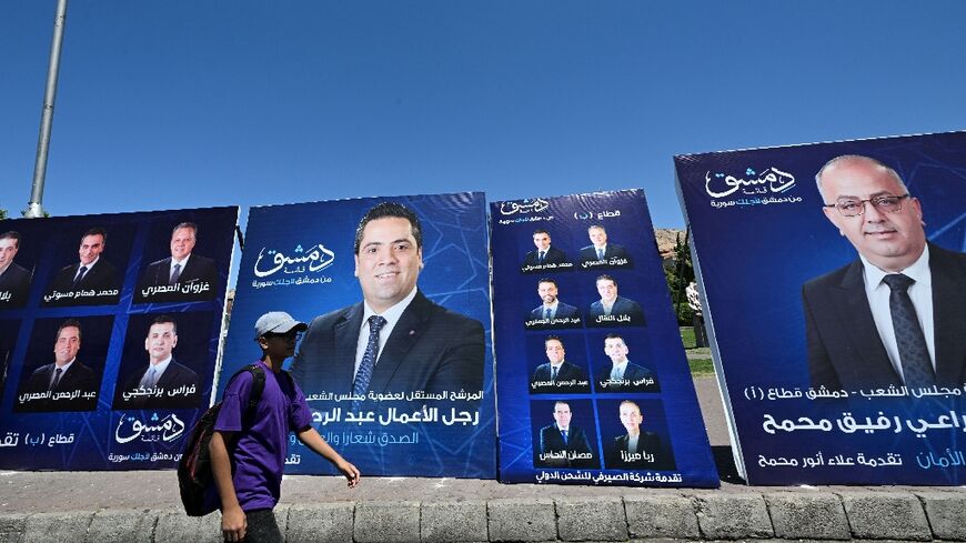 A young man walks past electoral campaign posters in Damascus a day ahead of parliamentary elections in government-held areas of Syria