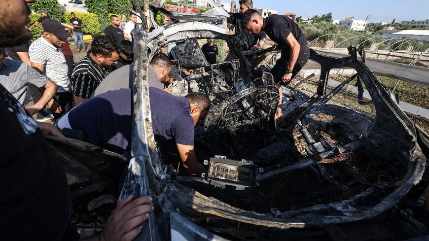 People near Tulkarem in the occupied West Bank check the remains of a car reportedly hit by an Israeli drone strike, which Palestinian sources said killed five people