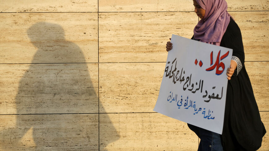 A woman walks holding a placard as activists demonstrate against female child marriages, in Tahrir Square in central Baghdad on July 28, 2024, amid parliamentary discussion over a proposed amendment to the Iraqi Personal Status Law. (Photo by AHMAD AL-RUBAYE / AFP) (Photo by AHMAD AL-RUBAYE/AFP via Getty Images)