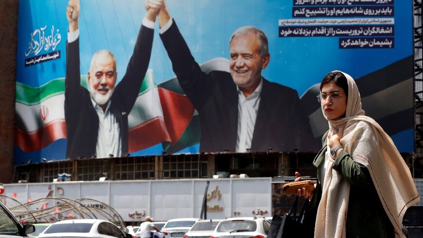 A woman walks past a picture of Iranian President Masoud Pezeshkian (R) and slain Hamas leader Ismail Haniyeh in Tehran