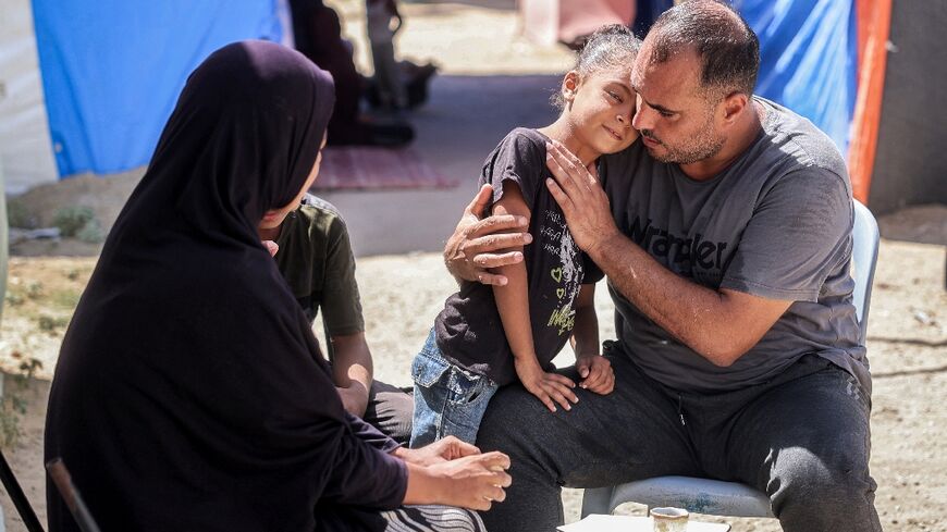 Maher Zino, 39, sits with his wife and children for coffee outside their tent at a makeshift camp in the central Gaza Strip