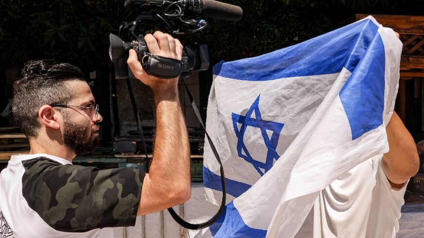 (FILES) An Israeli right-wing activist holds up an Israeli national flag to obscure the camera of a video journalist during the Jerusalem Day flag march