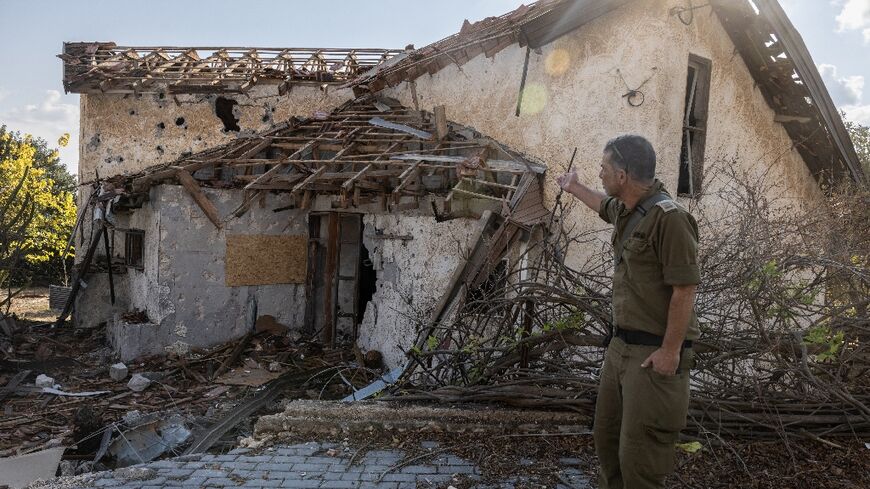 An Israeli soldier points at a house hit by Hezbollah rocket fire in the deserted northern Israeli town of Metula