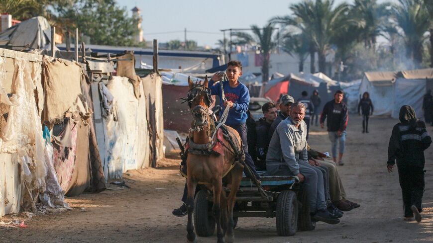 Displaced Palestinians using animal-drawn carts pass flimsy shelters in Al-Zawayda, central Gaza