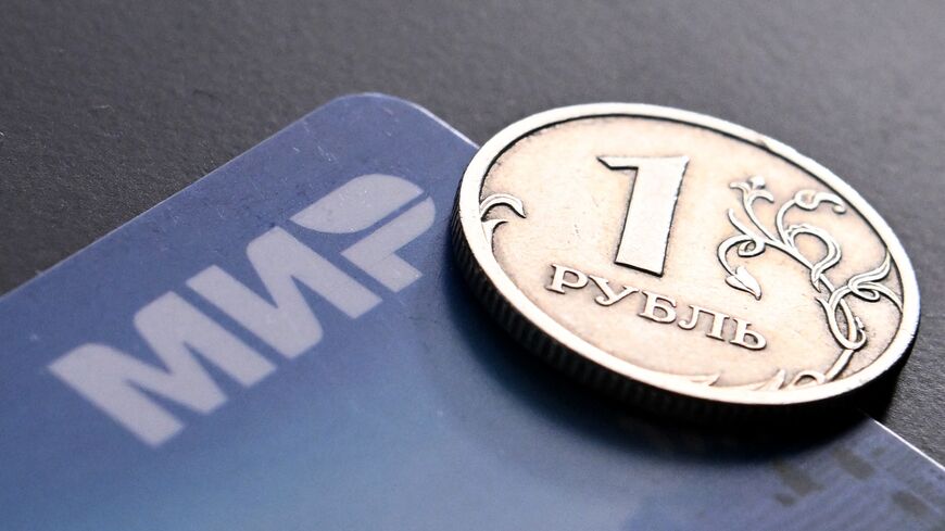 A photo taken on March 14, 2022, shows a Russian ruble coin and the Russian Mir payment system logo on a bank card in Moscow.