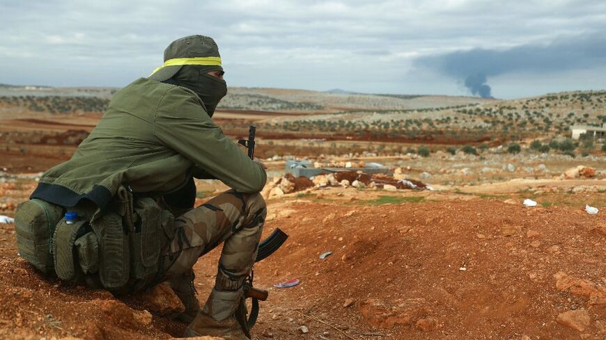 A fighter from Hayat Tahrir al-Sham (HTS) mans a position in the eastern outskirts of Atarib town, in Syria's Aleppo province, as smoke rises in the distance during clashes with the Syrian army