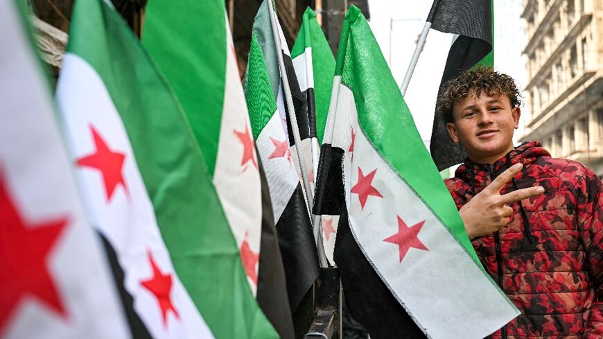 A man poses next to Syrian independence-era flags for sale at a stall in Aleppo city