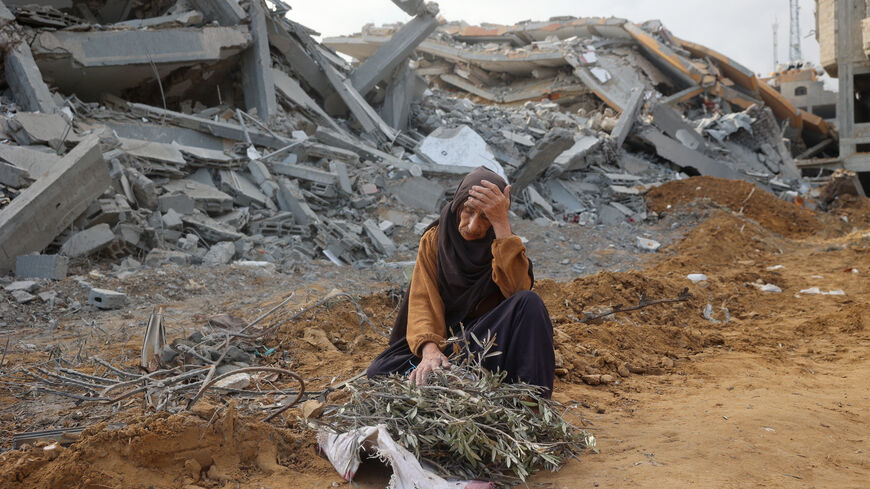 TOPSHOT - A elderly woman sits in front of a destroyed building to take a rest as she collects tree branches to light a fire in Nuseirat in the central Gaza Strip after Israeli shelling of the camp stopped on November 29, 2024, amid the ongoing war in the Palestinian territory between Israel and Hamas. (Photo by Eyad BABA / AFP) (Photo by EYAD BABA/AFP via Getty Images)