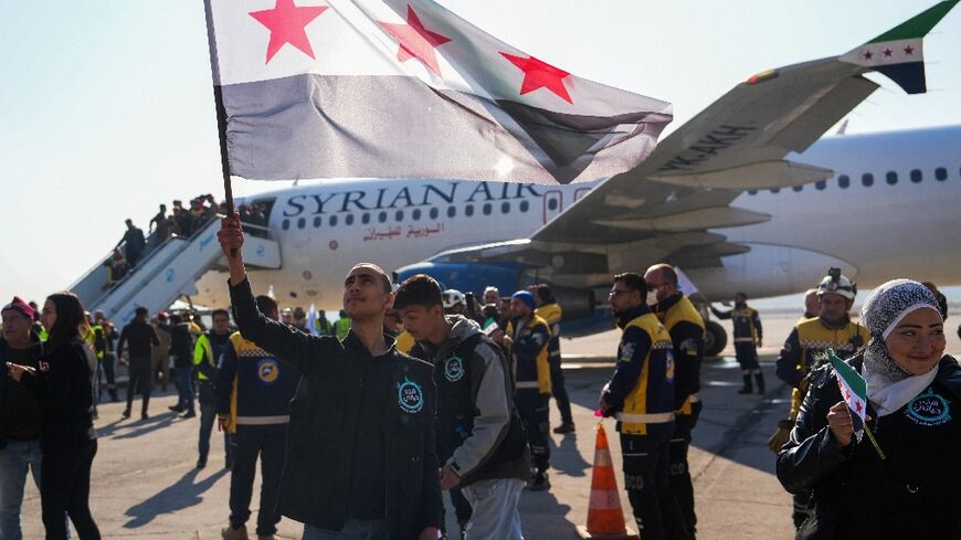 A man lifts an independence-era Syrian flag as passengers disembark in Aleppo, after the first commercial flight since Assad's ouster