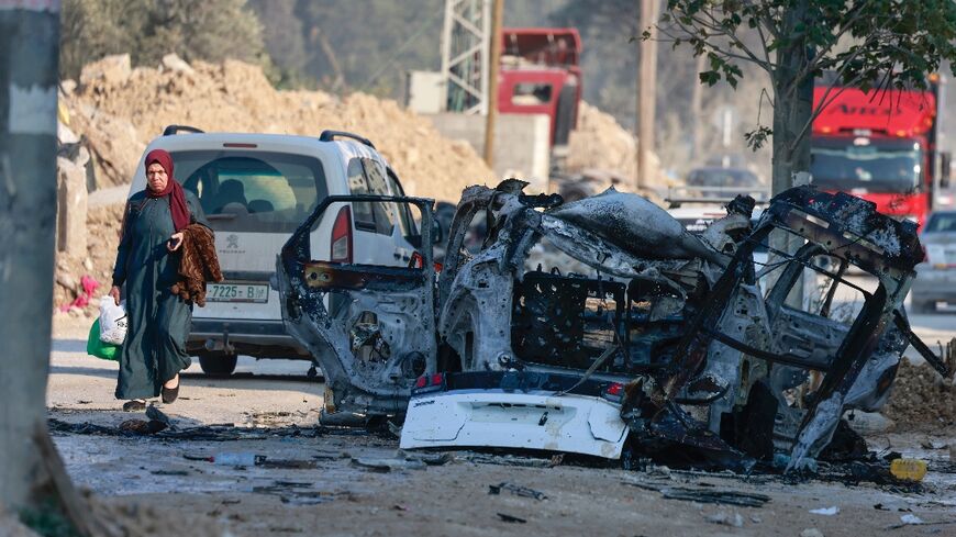 Palestinians drive their vehicles past the carcass of a car that was destroyed in an Israeli airstrike in the Nur Shams refugee camp near Tulkarem in the occupied West Bank