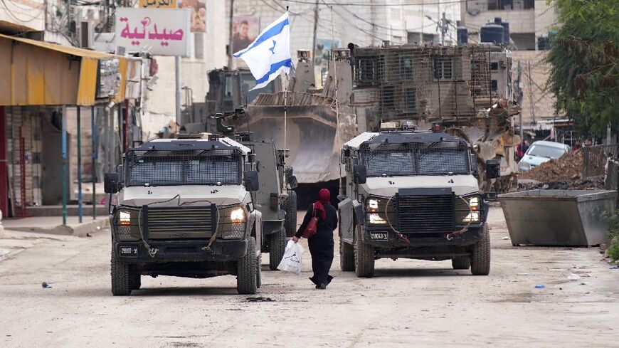 A Palestinian woman walks past Israeli army vehicles during a military raid in Jenin in the occupied West Bank