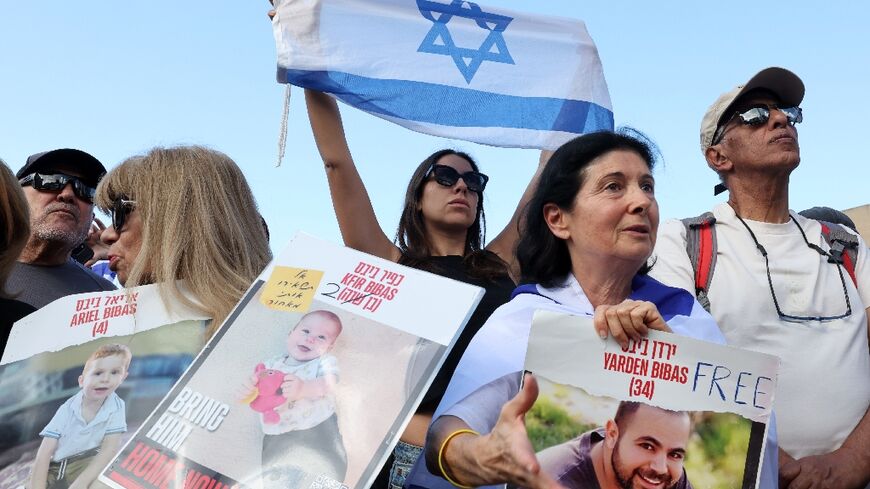 Onlookers with pictures of released hostage Yarden Bibas, as well as of his two children Kfir and Ariel