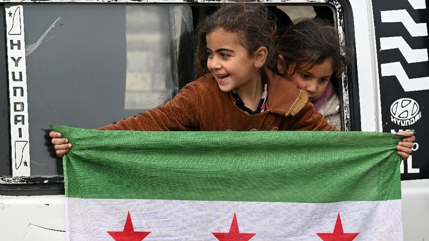 A girl holds an independence-era Syrian flag out of the window of a bus at the entrance to the central city of Homs