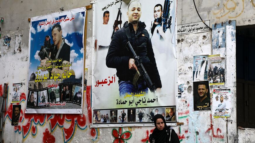 A Palestinian woman stands against a wall plastered with posters picturing "martyrs" at a market in the Balata camp, near the occupied West Bank city of Nablus, on Dec. 15, 2020.