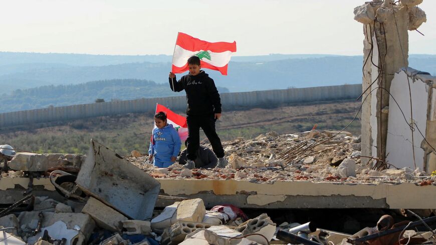 Lebanese children hold their national flag as they walk above the rubble of a destroyed building as families return with the Lebanese army to the southern village of Marwahin, near a border fence with Israel, on Jan. 28, 2025. 