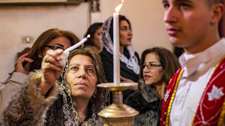 A woman reaches to light her candle from another held by deacon during the Christmas morning mass at the Syriac Orthodox Church of Virgin Mary in the Kurdish-majority city of Qamishli in Syria's northeastern Hasakeh province on Dec. 25, 2022.