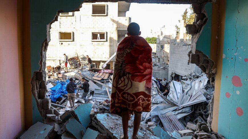 A youth draped in a blanket looks on as people look for survivors in the rubble of a building hit in an Israeli strike in the Bureij camp