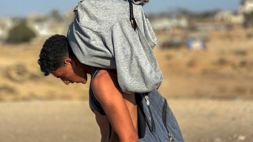 A youth walks with a package on his back as displaced Palestinians receive food packages from a US-backed foundation pledging to distribute aid in western Rafah in the southern Gaza Strip