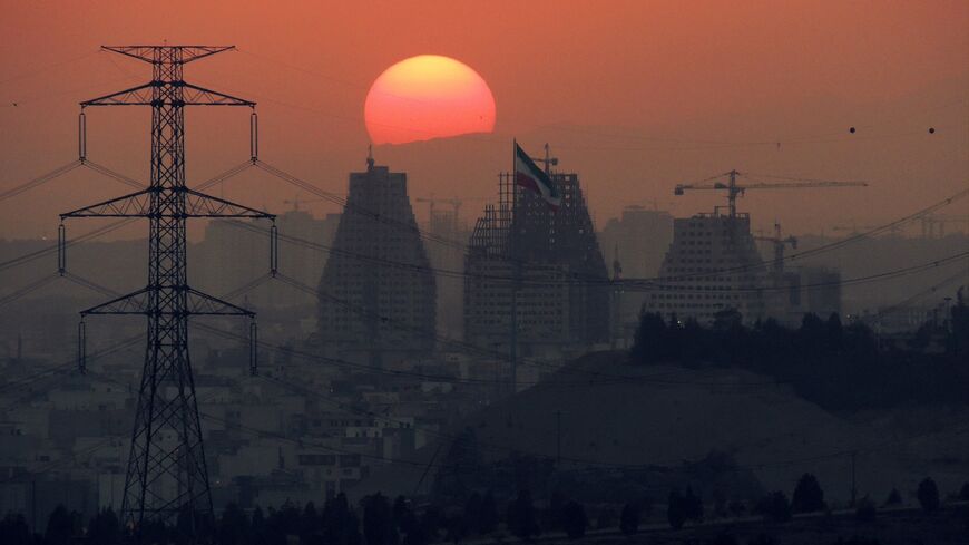Sun setting at the back of large buildings under construction of Tehran at dusk.