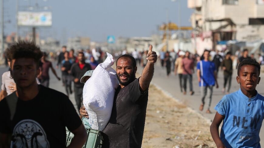 A man carries a bag of food aid while others rush to get a share after people stormed a World Food Programme warehouse in Deir el-Balah in Gaza on May 28, 2025