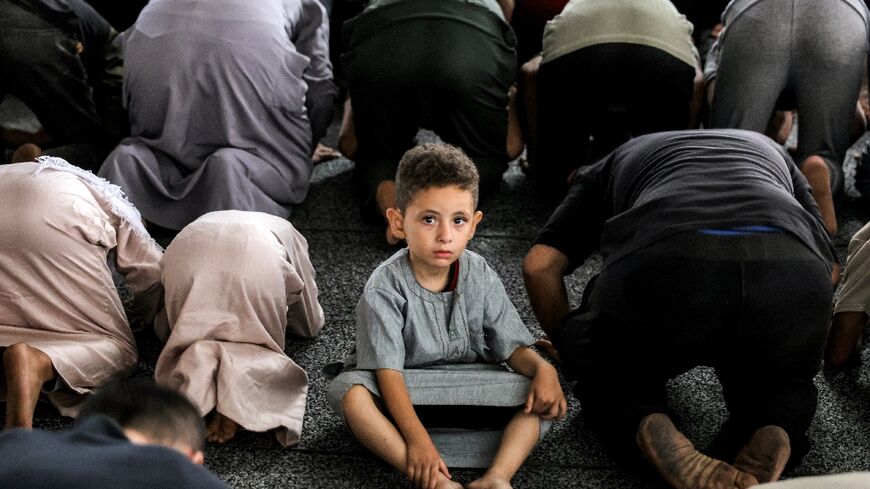 A boy looks on as he sits between Muslim worshippers prostrating as they perform the early morning prayers for Eid al-Adha at the makeshift prayer room of the Nour mosque in Gaza City