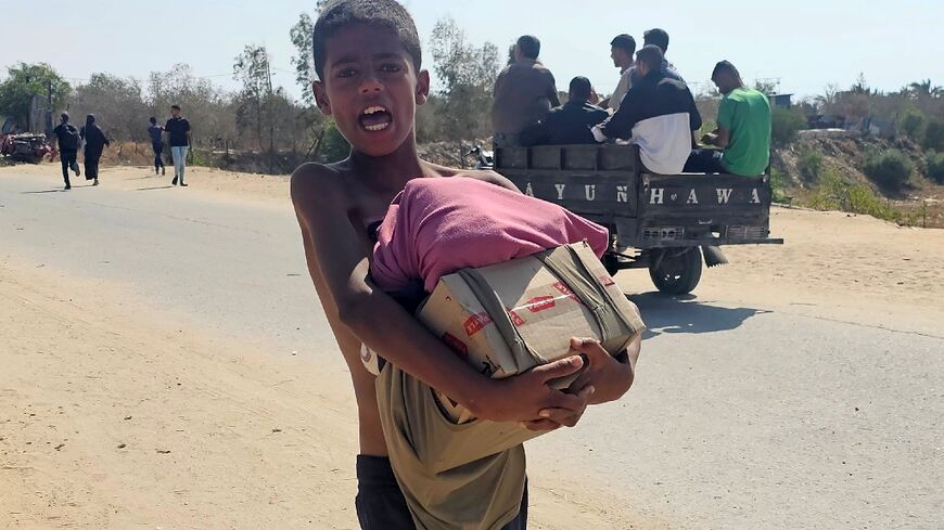 A boy walks with humanitarian aid relief packages as displaced Palestinians receive aid from a US-backed foundation in Rafah in southern Gaza