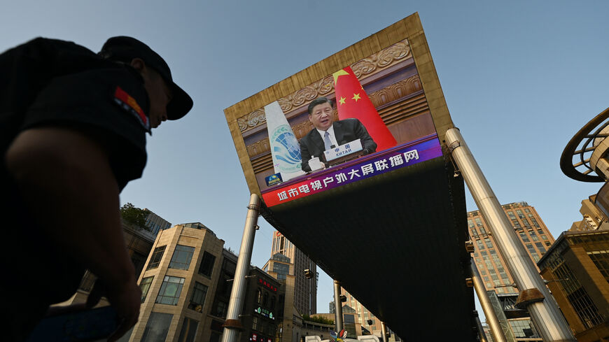 A security guard stands below a giant screen showing news footage of China's President Xi Jinping speaking virtually to the Shanghai Cooperation Organization meeting, which was being held in India, at a shopping mall in Beijing on July 4, 2023.