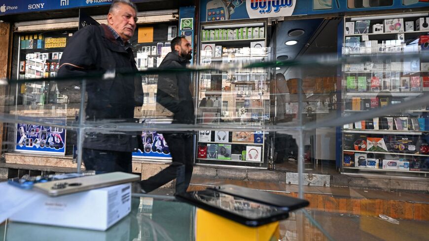 Men walk past shops selling mobile phones in the Damascus Tower market, which specializes in the smart phone business, in the Syrian capital on January 12, 2025. 