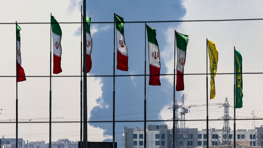 Flags flutter along a bridge as a plume of heavy smoke and fire rise from an oil refinery in southern Tehran, after it was hit in an overnight Israeli strike, on June 15, 2025. Iran fired a fresh barrage of missiles at Israel, state television announced early on June 15, as the rivals exchanged fire for a third day. (Photo by ATTA KENARE / AFP) (Photo by ATTA KENARE/AFP via Getty Images)