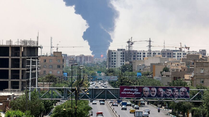 Portraits of Iranian military generals and nuclear scientists, killed in Israel's June 13 attack are displayed above a road, as a plume of heavy smoke and fire rise from an oil refinery in southern Tehran, after it was hit in an overnight Israeli strike, on June 15, 2025. 