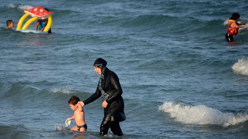 A Tunisian woman wearing a "burkini", a full-body swimsuit designed for Muslim women, walks in the water with a child on August 16, 2016 at Ghar El Melh beach near Bizerte, north-east of the capital Tunis. (Photo by FETHI BELAID / AFP) (Photo by FETHI BELAID/AFP via Getty Images)