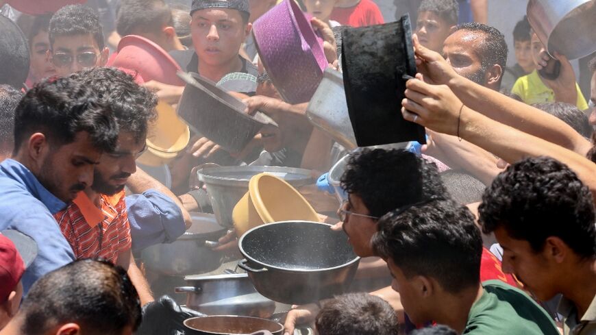 Palestinians try to get food at a charity kitchen providing hot meals in Gaza City