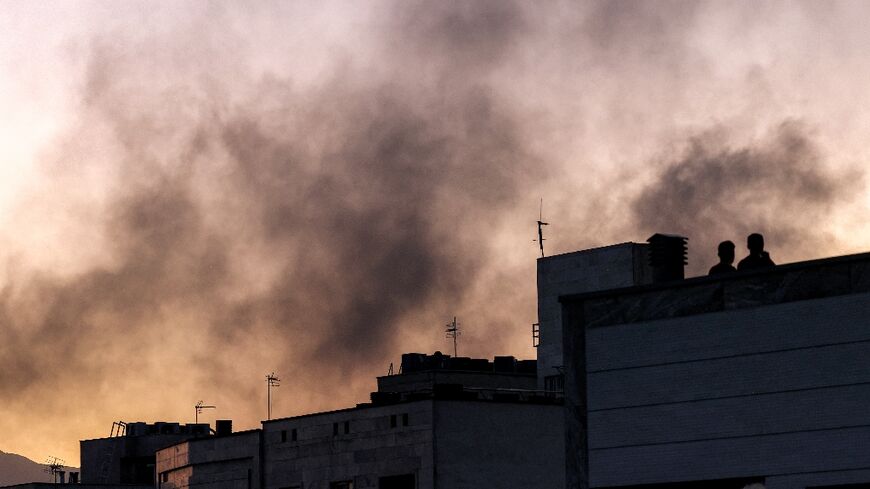 People stand on a rooftop as smoke wafts over Tehran following an Israeli strike