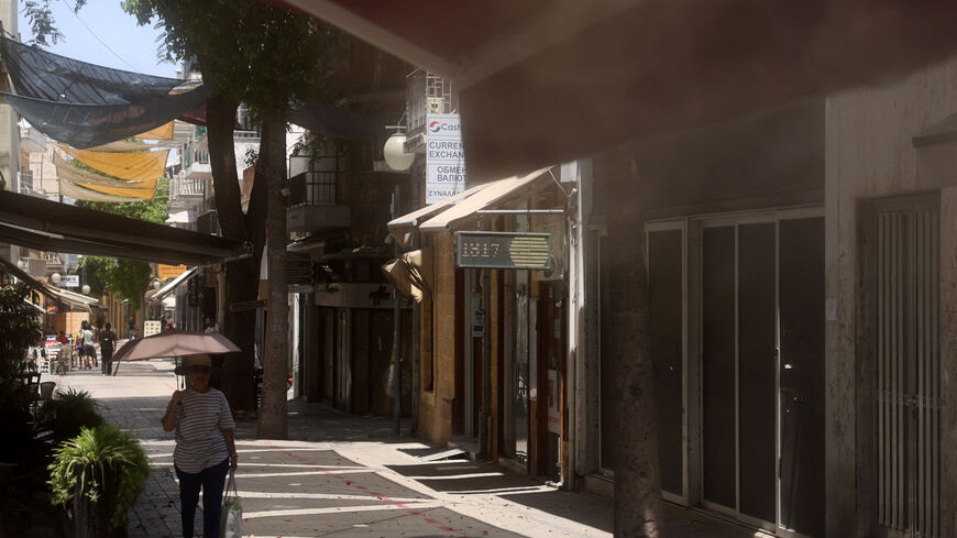 A woman shelters from the sun with an umbrella while a mist machine works at a coffeshop during a heatwave in Nicosia, Cyprus July  23, 2025. REUTERS/Yiannis Kourtoglou
