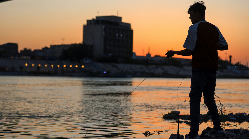 An Iraqi boy catches fish in the Tigris River in central Baghdad as the sun sets, on April 15, 2025.